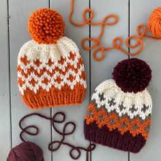 two knitted hats sitting on top of a white wooden table next to yarn and scissors