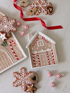 gingerbread house and ginger cookies with red ribbon on white table top next to candy canes