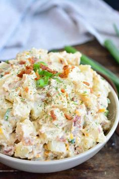 a white bowl filled with potato salad on top of a wooden table next to green beans