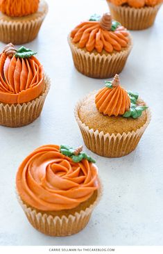 cupcakes with frosting and pumpkin decorations are arranged on a white countertop