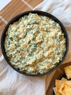 spinach dip in a black bowl next to tortilla chips on a table