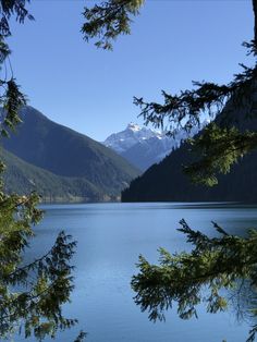 a lake surrounded by mountains and trees with snow on the mountain tops in the distance