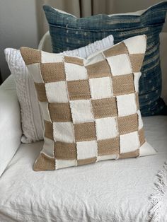 a white couch with two pillows on it and one is brown and white checkerboard