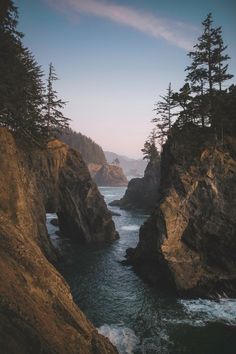 the ocean is surrounded by large rocks and pine trees