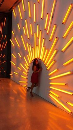 a woman standing in front of a wall with yellow lights on it and her arms behind her back