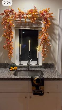 a kitchen sink under a mirror next to a window with candles and flowers on it