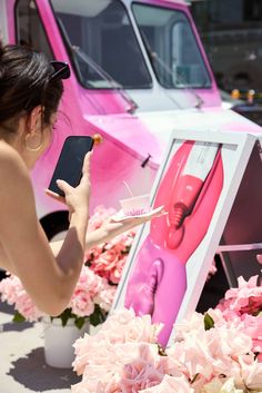 a woman holding a cell phone in front of a pink truck with flowers on it