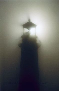 a lighthouse in the fog with a light shining on it