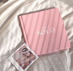 an open pink album sitting on top of a bed next to a polaroid photo