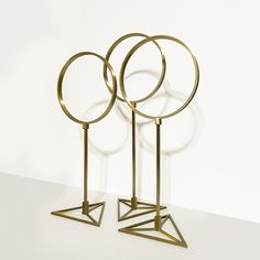 three circular and triangular brass sculptures on pedestals against a white wall with glass balls in the background