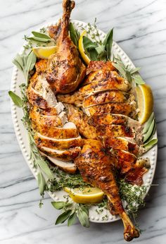 roasted chicken with herbs and lemons on a white platter over marble counter top