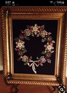 a gold frame with a wreath made out of flowers and pearls on it, sitting on a wooden floor