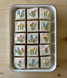 several square pieces of cake with flowers on them in a white dish sitting on a wooden table