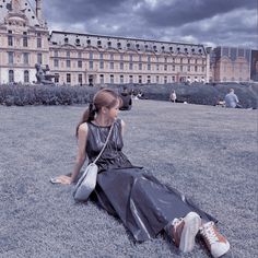 a woman sitting on the grass in front of a large building