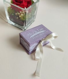 a small box with a flower in it next to a glass vase filled with flowers