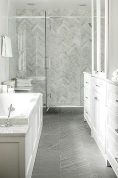 a white bathroom with gray tile flooring and large walk in shower next to the tub