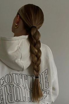 a woman with long hair wearing a white sweatshirt and gold hoop earrings, standing in front of a wall