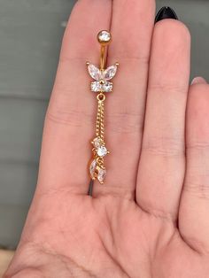 a person is holding a gold and white diamond butterfly belly ring in their left hand