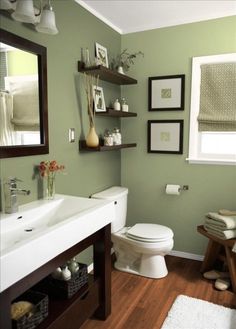 a white toilet sitting next to a sink in a bathroom under a window with pictures on the wall