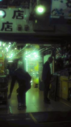 two men are standing in the middle of a train station at night, one is holding an umbrella