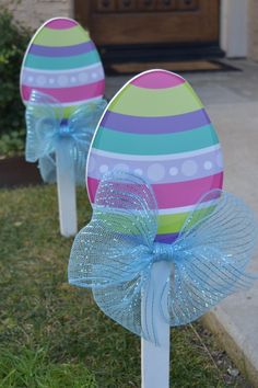 two decorated easter eggs sitting on top of white poles in the grass next to a door