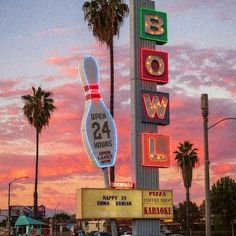 a neon bowling ball sign on the side of a building with palm trees in the background