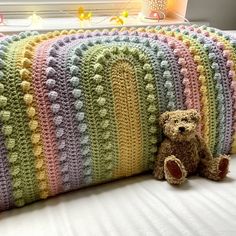 a teddy bear sitting next to a crocheted pillow