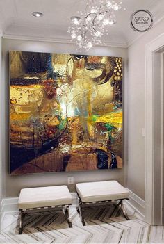 a large painting hanging on the wall in a room with two stools and a chandelier