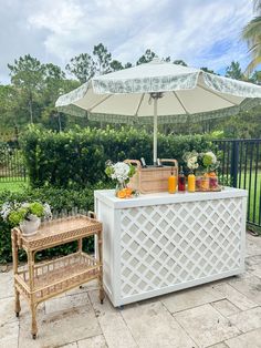 a white bar with an umbrella and some drinks on it next to a fenced in area