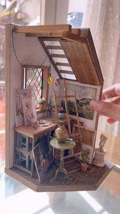 someone is holding up a miniature dollhouse in their hand, with pictures on the wall