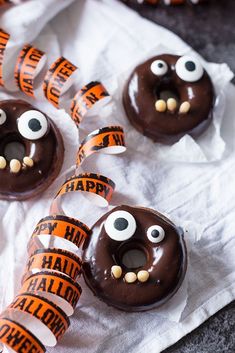 chocolate covered donuts decorated with fake eyes and orange tape are on a white napkin