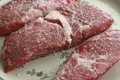 three pieces of raw meat on a plate with salt sprinkled on top and one piece cut out