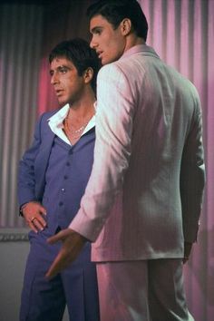 two men standing next to each other in front of a pink wall with curtains behind them