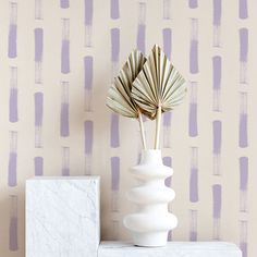 a white vase sitting on top of a table next to a wallpapered wall