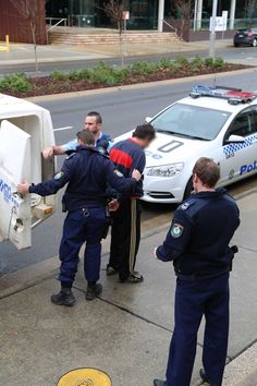 three police officers are standing on the sidewalk near a white refrigerator that is being opened