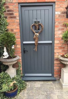 a grey door with a heart shaped wreath on the top and two planters next to it