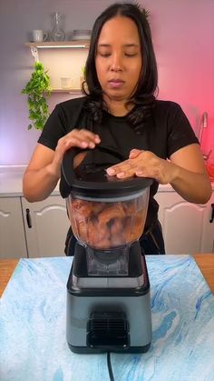 a woman standing in front of a blender filled with food on top of a table