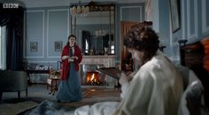 a woman standing in a living room next to a fire place