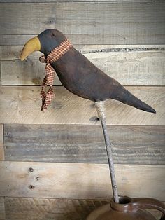 an old wooden bird on top of a potted plant in front of a wood paneled wall