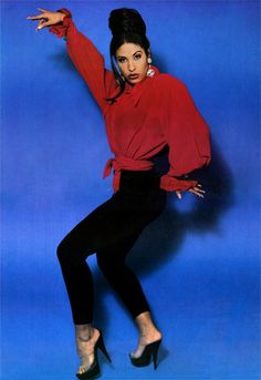 a woman in red shirt and black pants posing with her arms out, wearing high heels