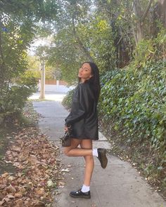 a woman walking down a sidewalk next to trees