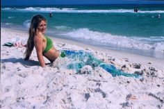 a woman in a green bathing suit sitting on the beach next to some blue and white water