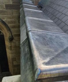 a cat is sitting on the edge of a metal gutter next to a brick building