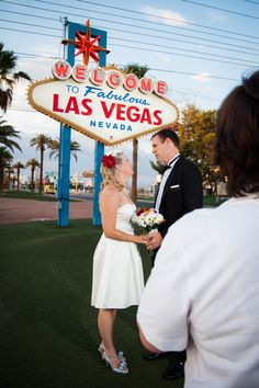 a bride and groom standing in front of the welcome sign to las vegas, nevada