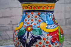 a colorful vase sitting on top of a metal table next to a brick wall,