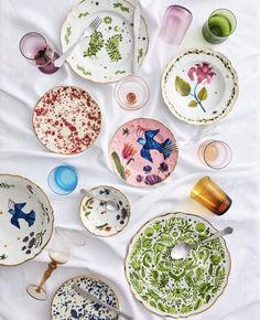 many different plates and cups on a white table cloth, with one plate in the middle