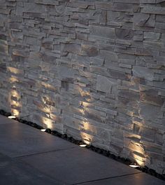 some lights that are on the side of a stone wall in front of a building