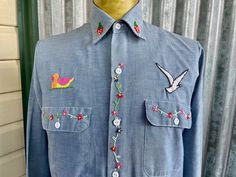 a blue shirt with embroidered birds and flowers on the chest, sitting on a mannequin's dummy