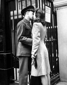 an old photo of a man and woman kissing on the street in front of a building