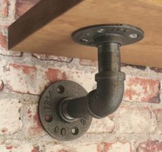 an industrial pipe is attached to the brick wall with a wooden shelf above it that holds a light fixture